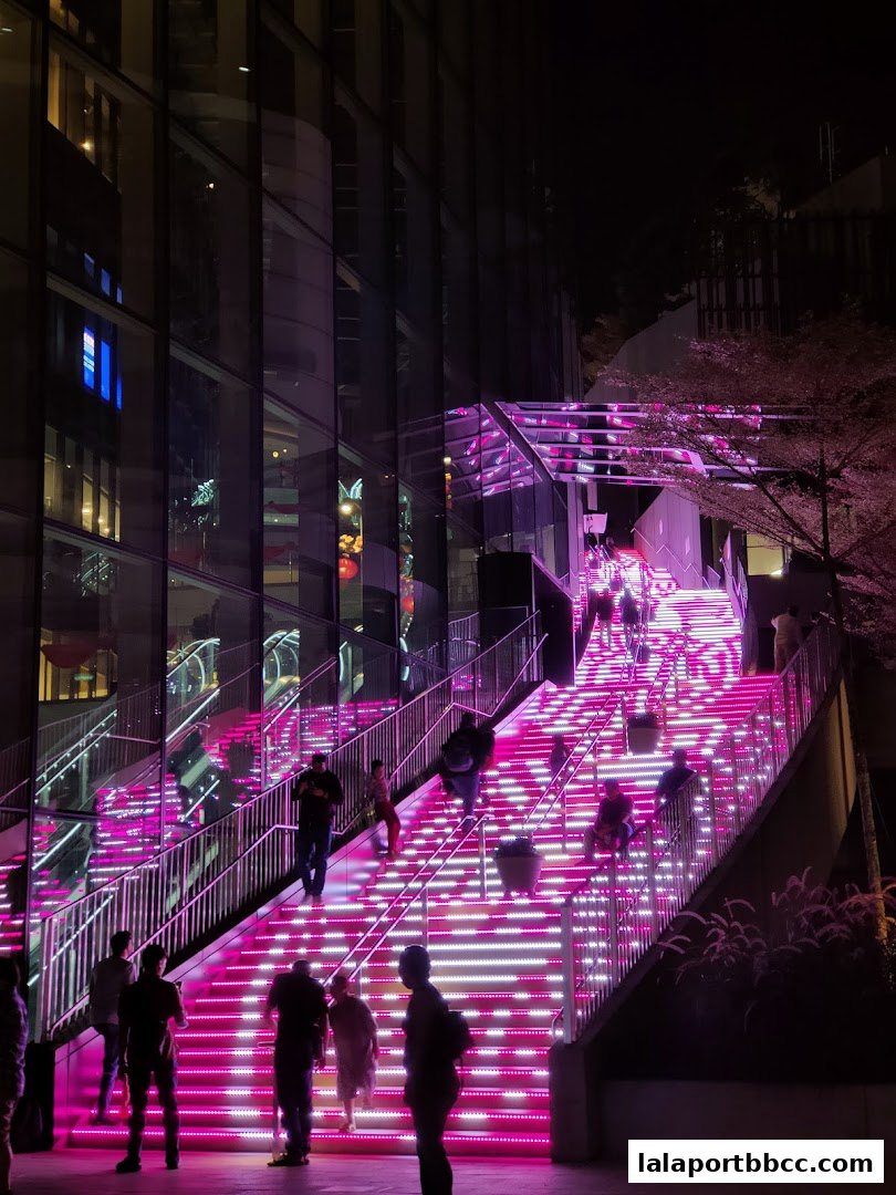 People ascend a brightly lit staircase with pink and white lights at night.