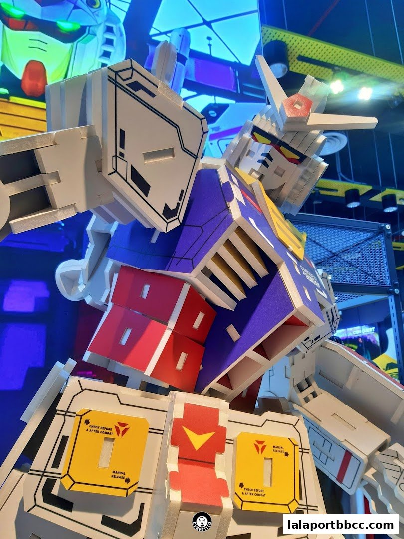 A close-up of a large, colorful Gundam model with intricate details and warning labels.
