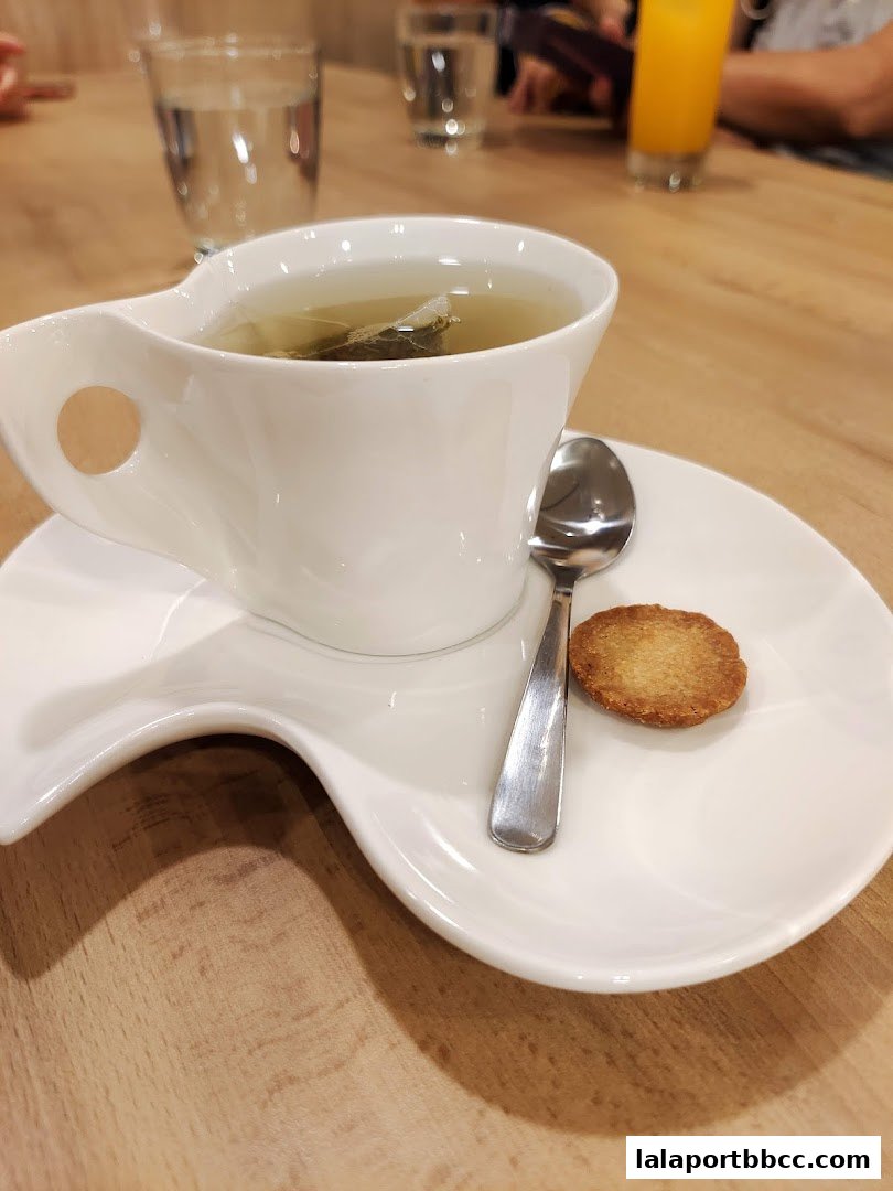 A close-up of a cup of tea with a biscuit and spoon on a saucer.