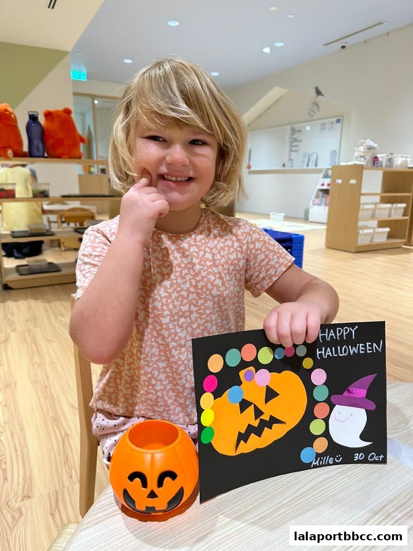 A smiling child holds a Halloween craft with a pumpkin and ghost.