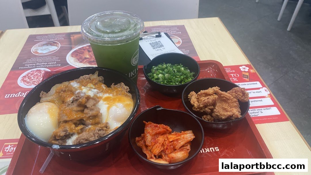 A Sukiya meal featuring a beef bowl, fried chicken, kimchi, chopped scallions, and a green drink.