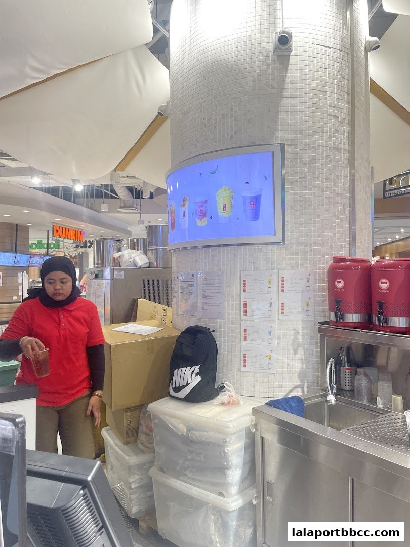A Gong Cha staff member stands behind a counter with drinks displayed on a screen.