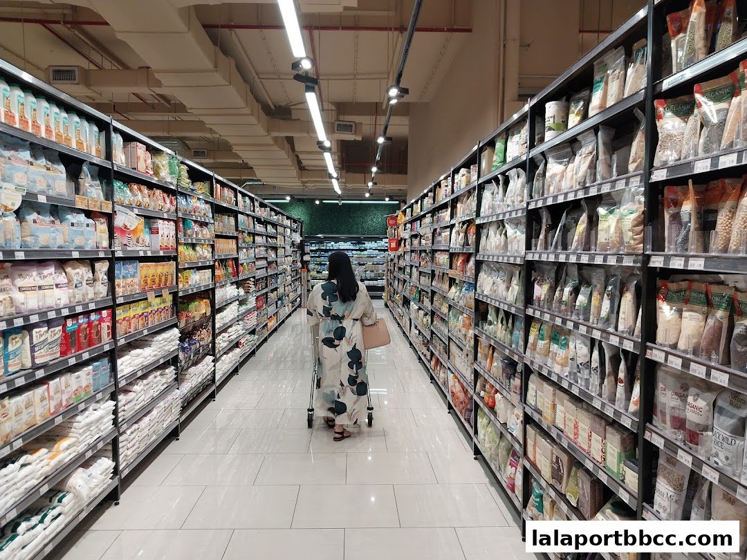 A person walks down a brightly lit aisle filled with shelves of groceries at Jaya Grocer.