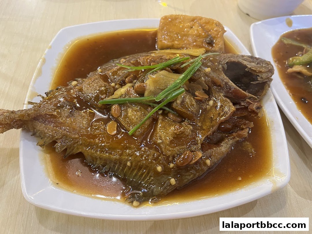 A close-up of a whole fried fish in a savory sauce with peanuts and green onions.