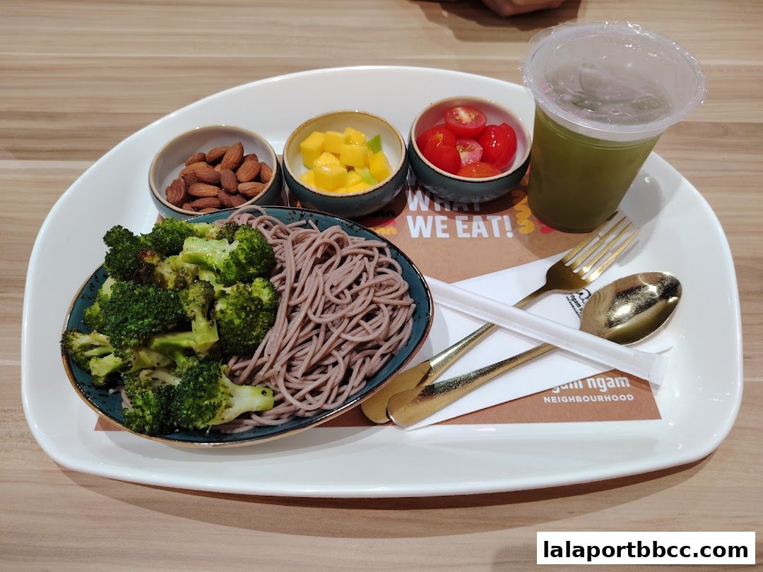A healthy meal with soba noodles, broccoli, almonds, mango, and cherry tomatoes, served with a green drink.