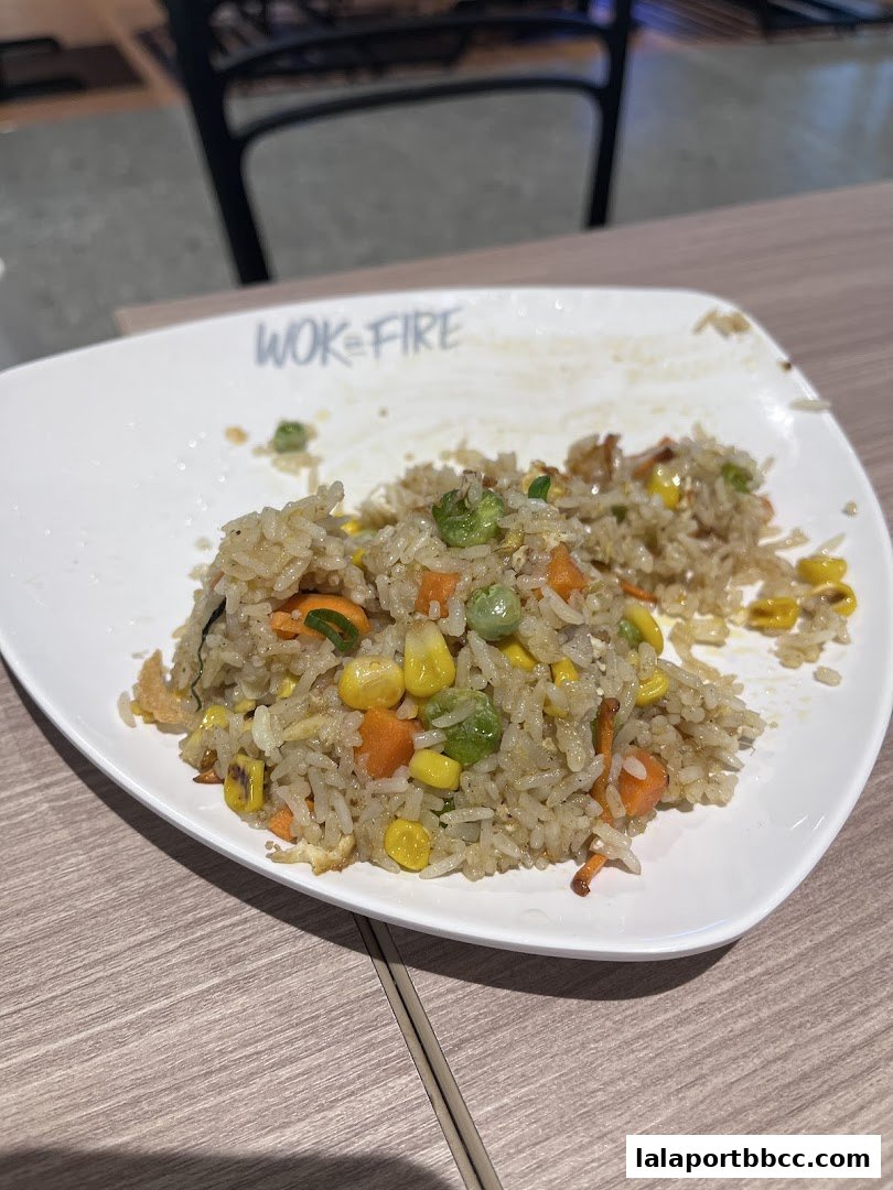 A plate of fried rice with vegetables on a wooden table.