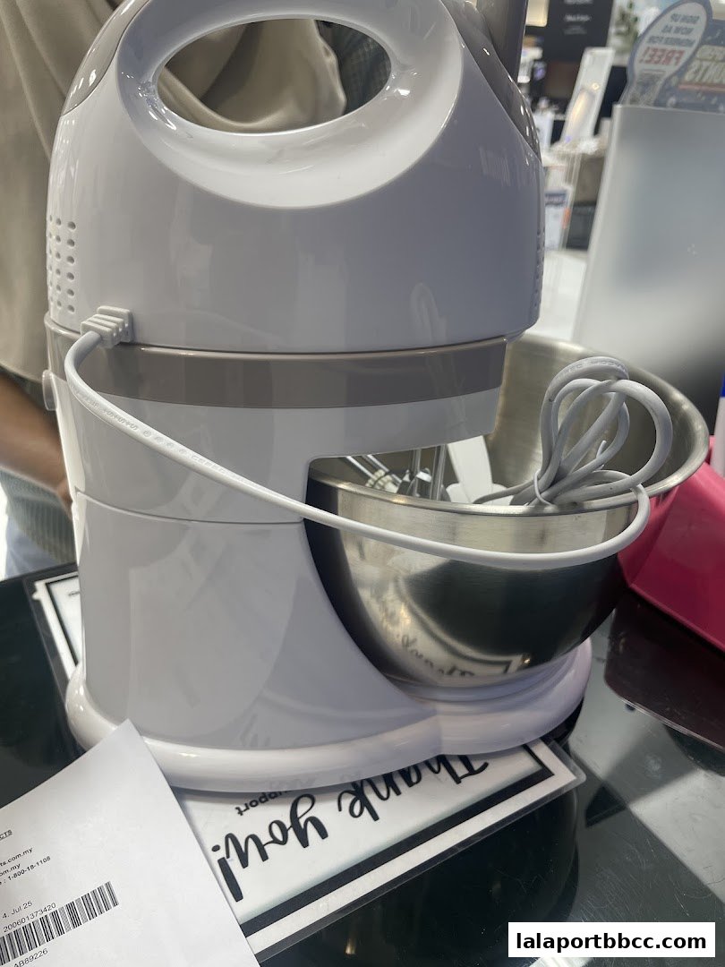 A white stand mixer with a stainless steel bowl and whisk attachments is displayed.