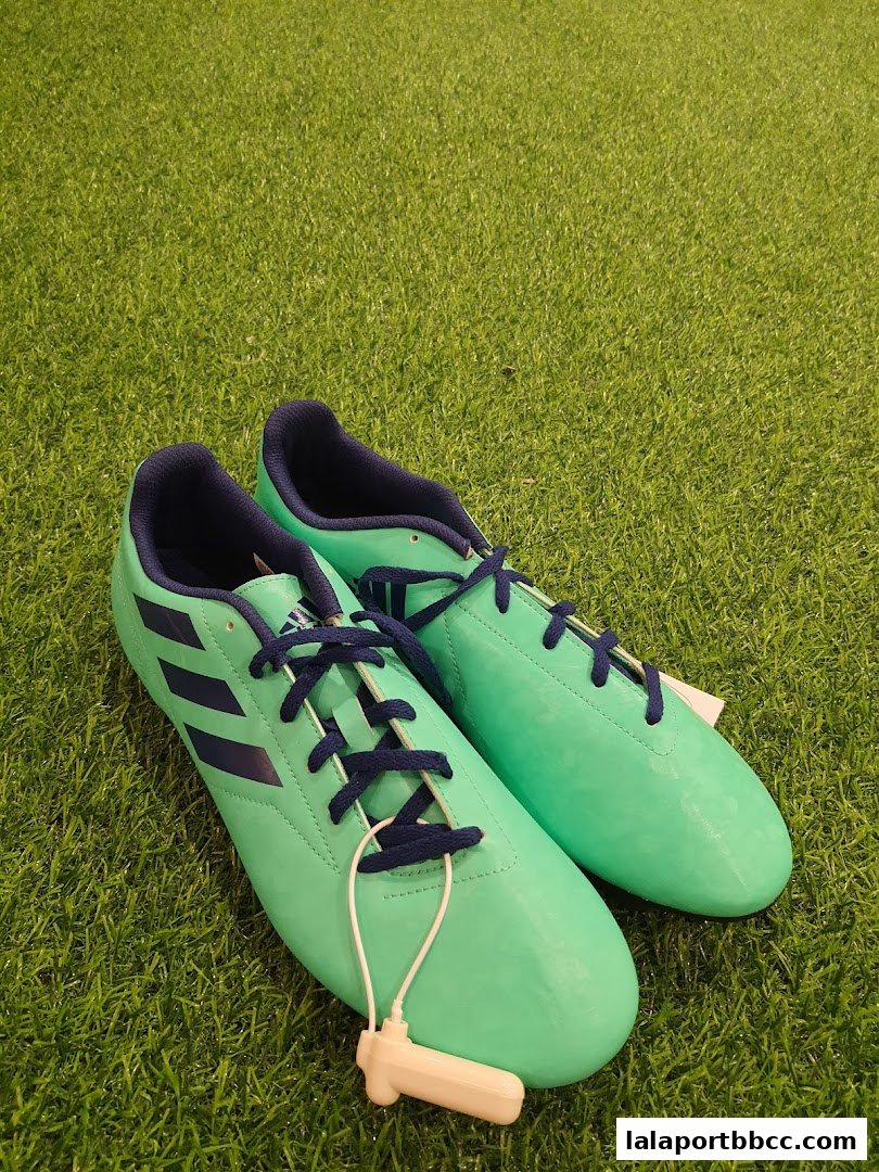 A pair of bright green Adidas soccer cleats with navy blue laces and stripes on a green grass background.
