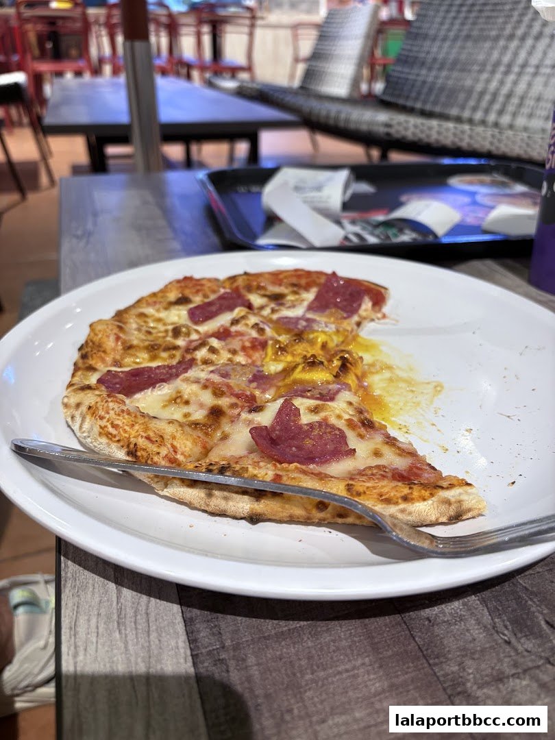 A slice of pizza with salami and cheese on a white plate with a fork.