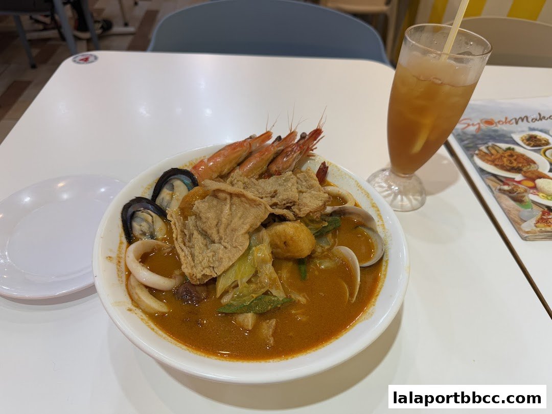 A bowl of seafood noodle soup with prawns, mussels, and squid, served with iced tea.