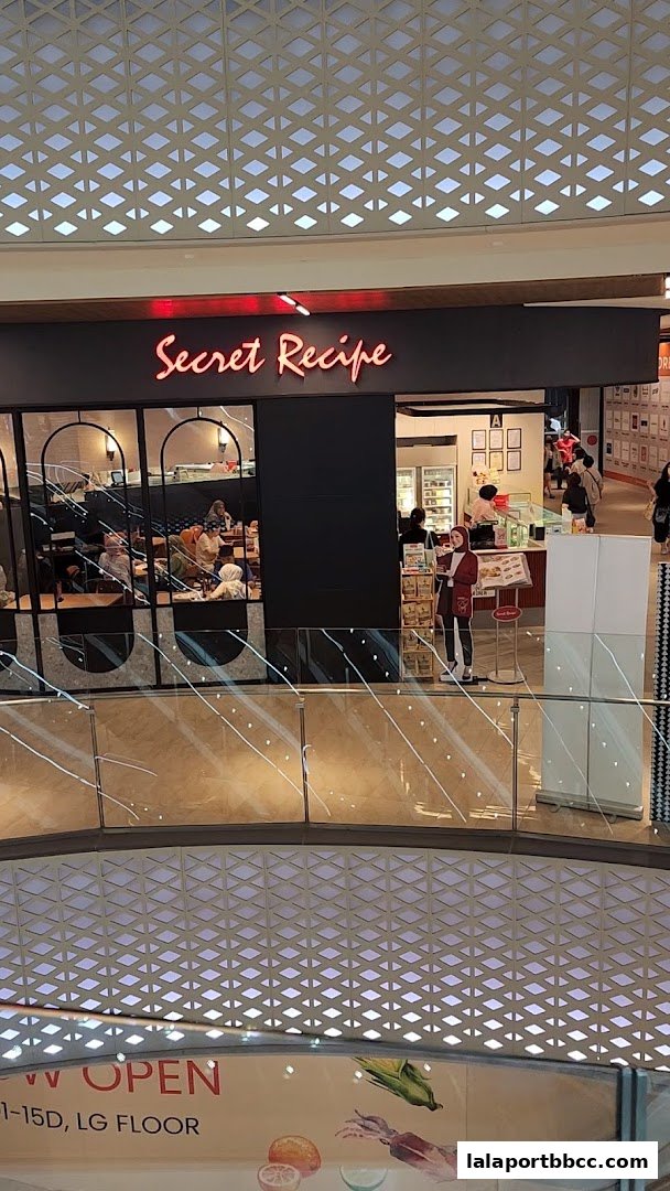 The exterior of a Secret Recipe cafe with customers seated inside and a display counter.