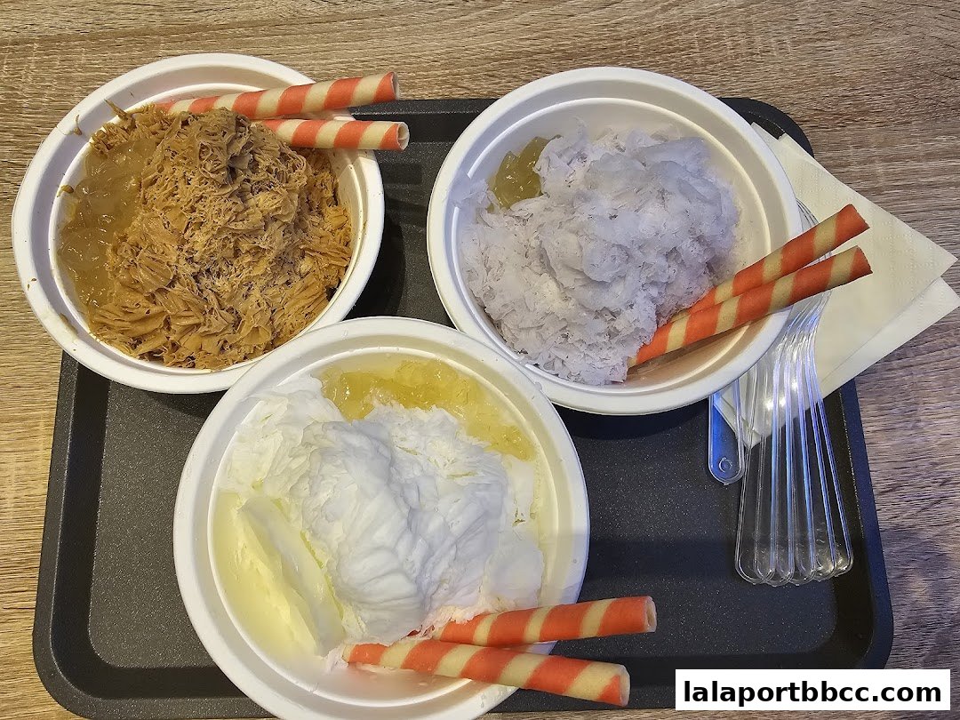 Three bowls of shaved ice desserts with wafer sticks and toppings on a tray.