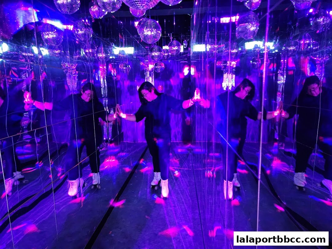 People roller skating in a mirrored room with disco balls and purple lighting.