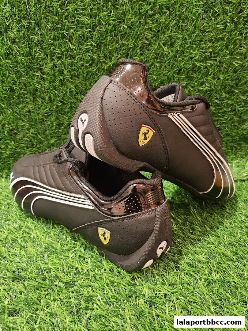 A pair of black Puma Ferrari racing shoes displayed on a green grassy surface.