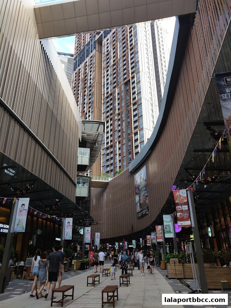 People walking through a modern outdoor shopping area with tall buildings in the background.