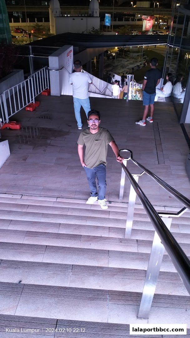 A man stands on a wide staircase at night, with other people walking up and down.