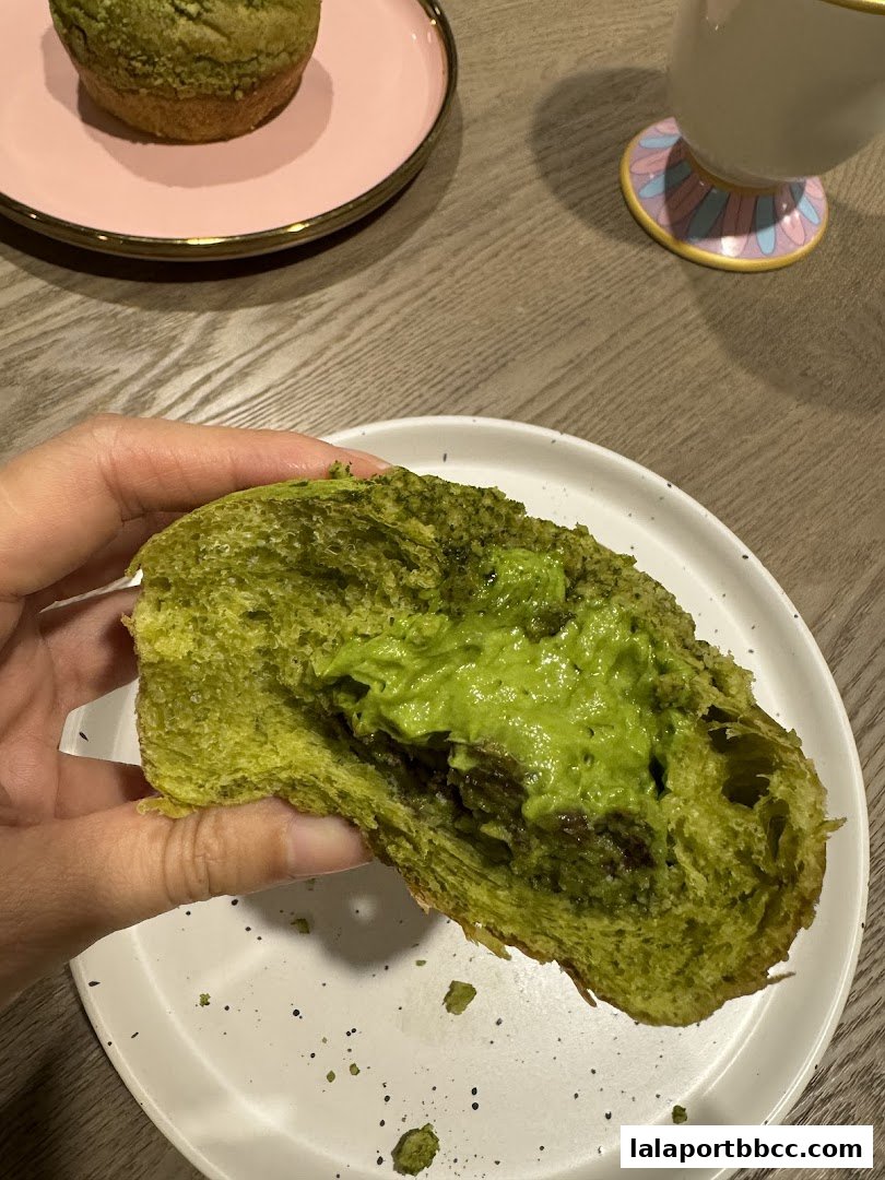 A hand holds a green matcha bread filled with creamy matcha filling.