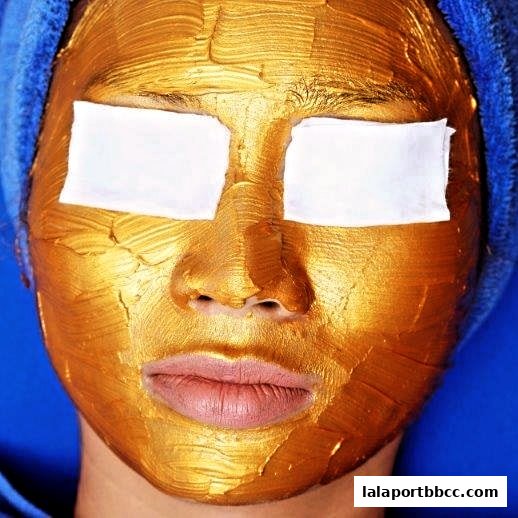 A close-up of a person's face covered in a golden facial mask with white eye patches.