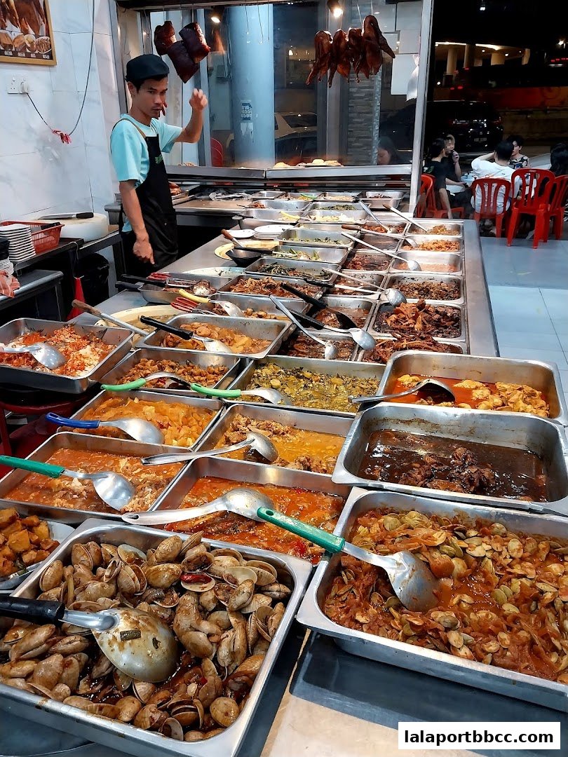 A wide selection of cooked dishes displayed in trays, with a server in the background.