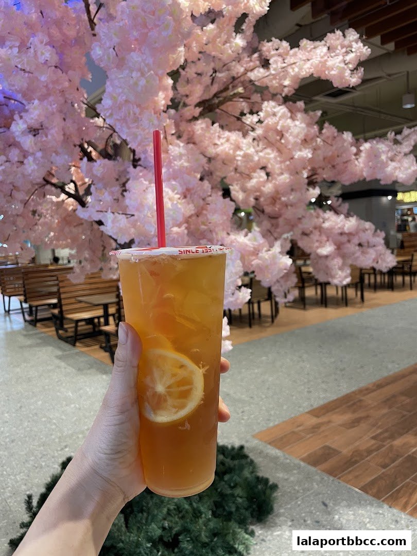 A hand holds a refreshing iced tea with lemon in front of a blooming cherry blossom tree.