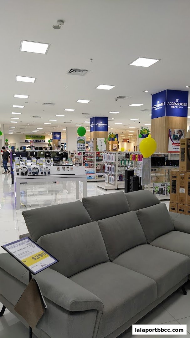 Interior view of a Nojima electronics store with a sofa in the foreground and various electronics on display.