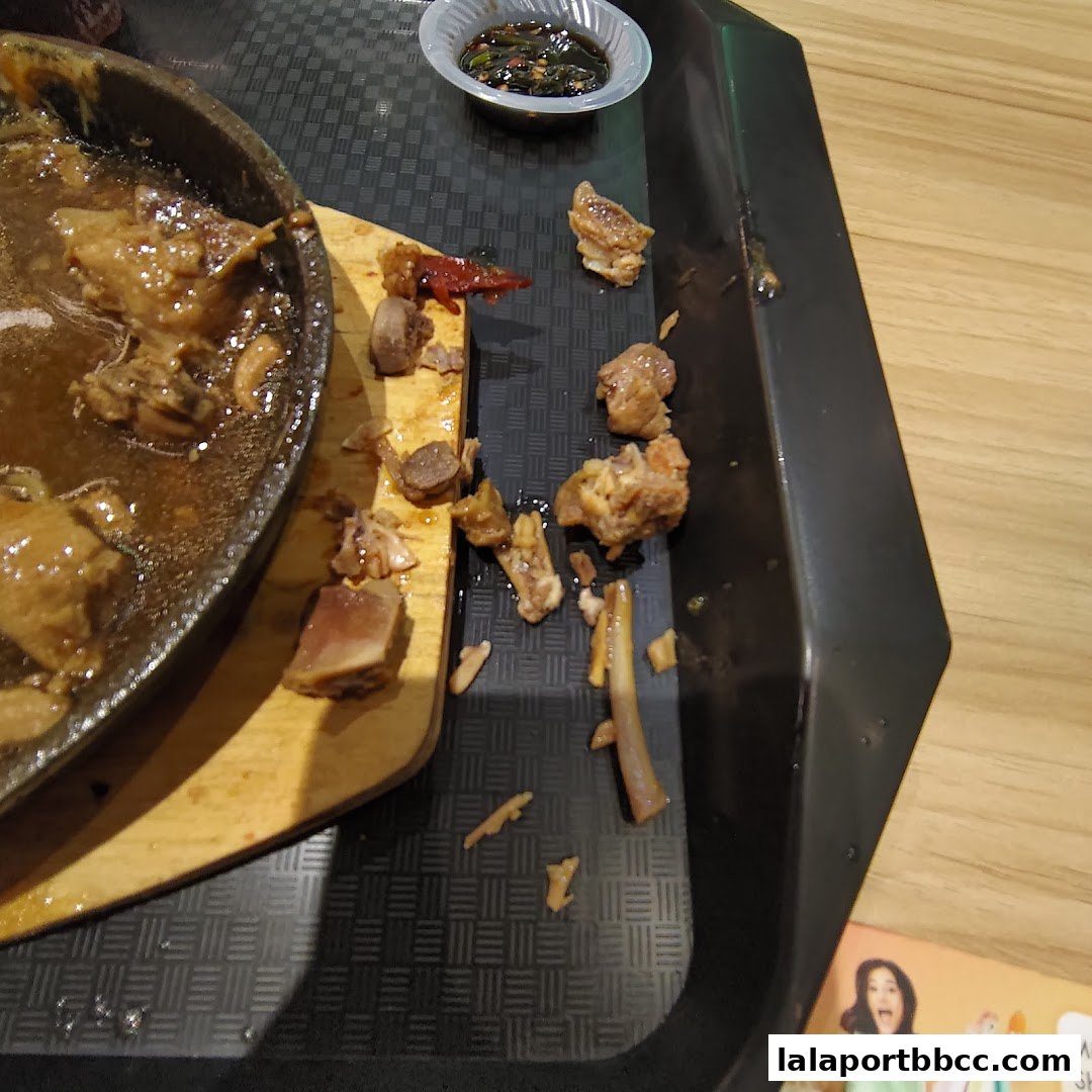 A close-up of a sizzling claypot dish with leftover bones and a dipping sauce.