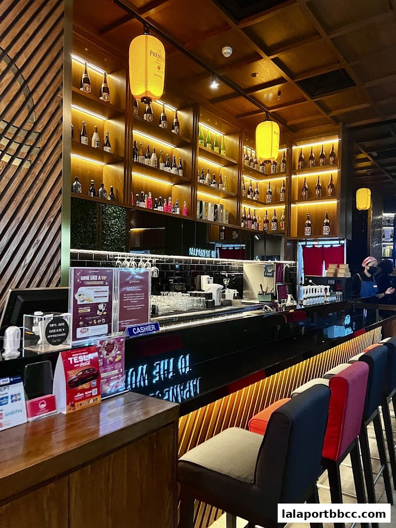Interior shot of a Japanese restaurant bar with shelves stocked with bottles and seating.