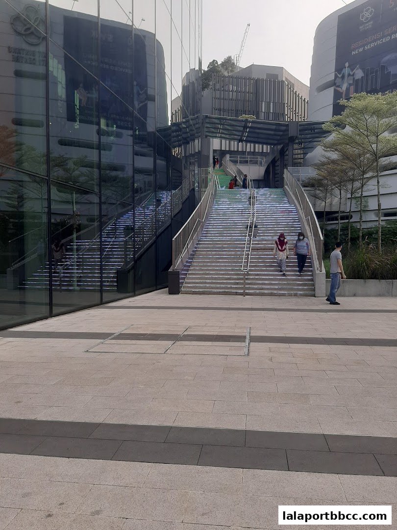 People walking up illuminated stairs at a modern shopping mall entrance.