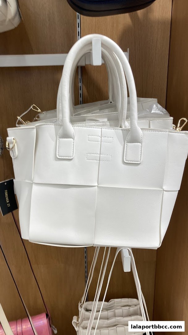 A white woven tote bag with top handles and a crossbody strap is displayed.