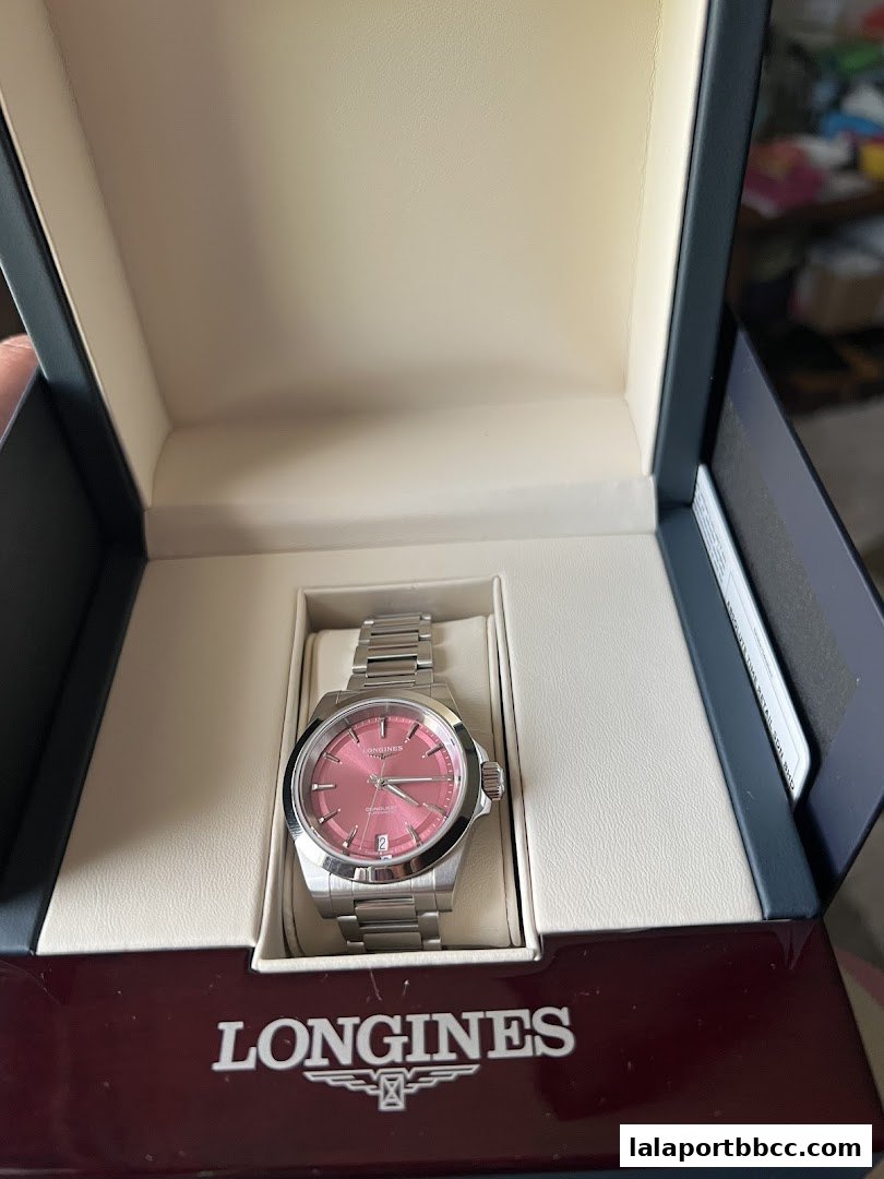 A Longines watch with a pink dial is displayed in its presentation box.