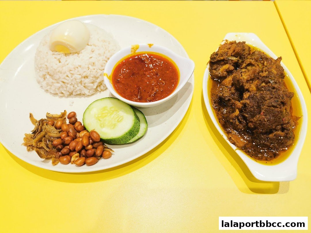 A plate of Nasi Lemak with chicken, rice, sambal, peanuts, anchovies, cucumber, and a boiled egg.
