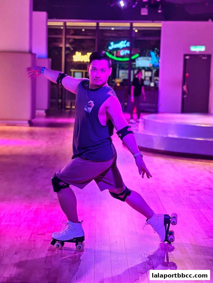 A man in roller skates poses on a wooden floor with purple lighting.