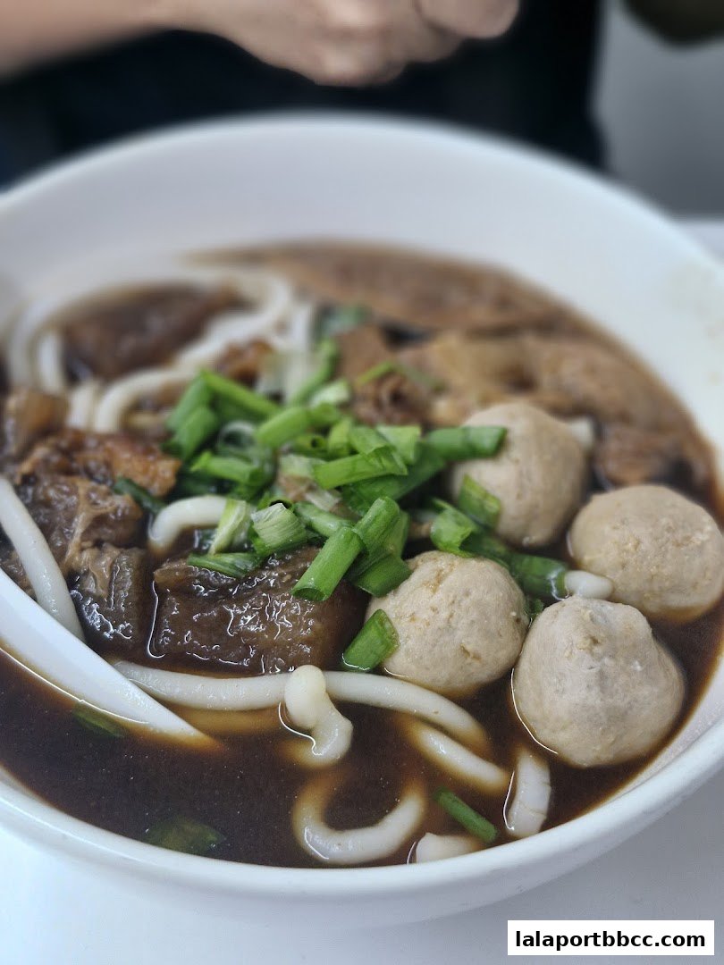 A close-up shot of a steaming bowl of Hong Kong-style noodles with beef and meatballs.