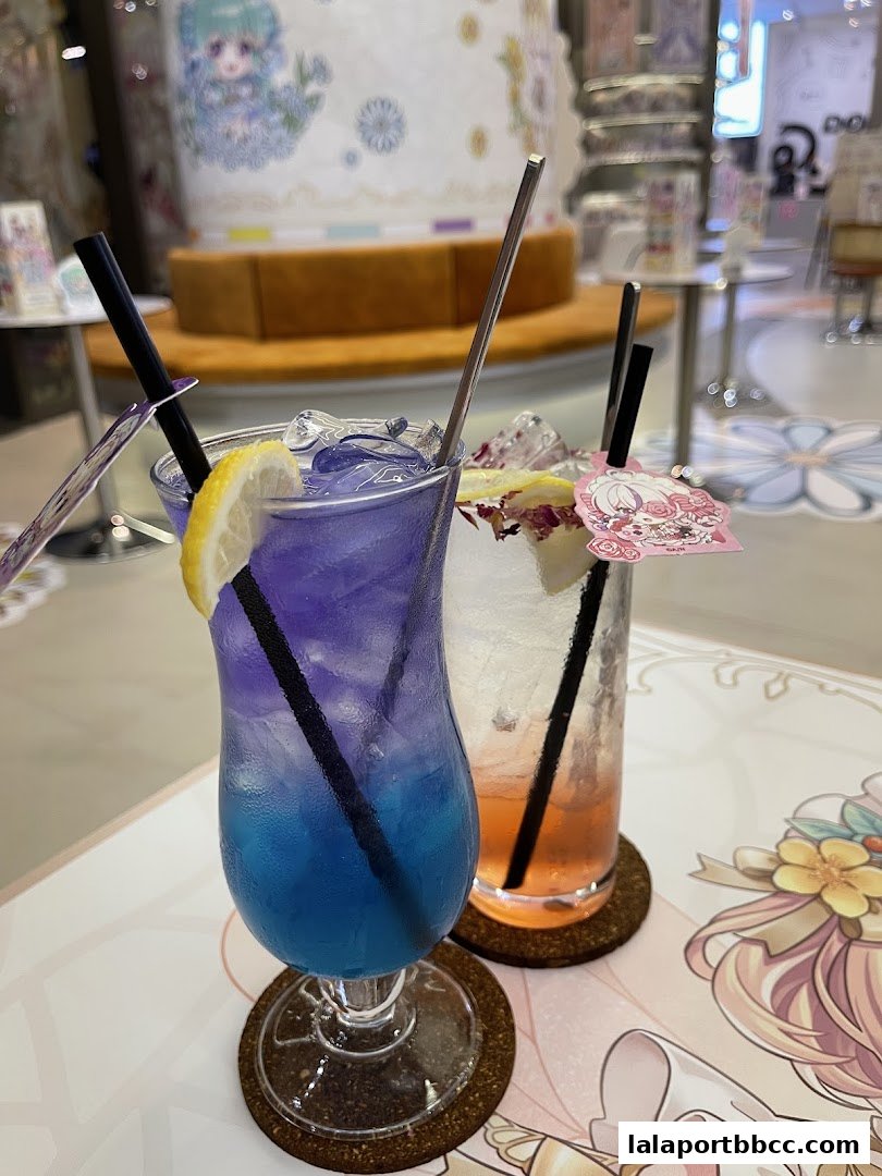 Two colorful drinks with lemon and straws on a table with a decorative print.