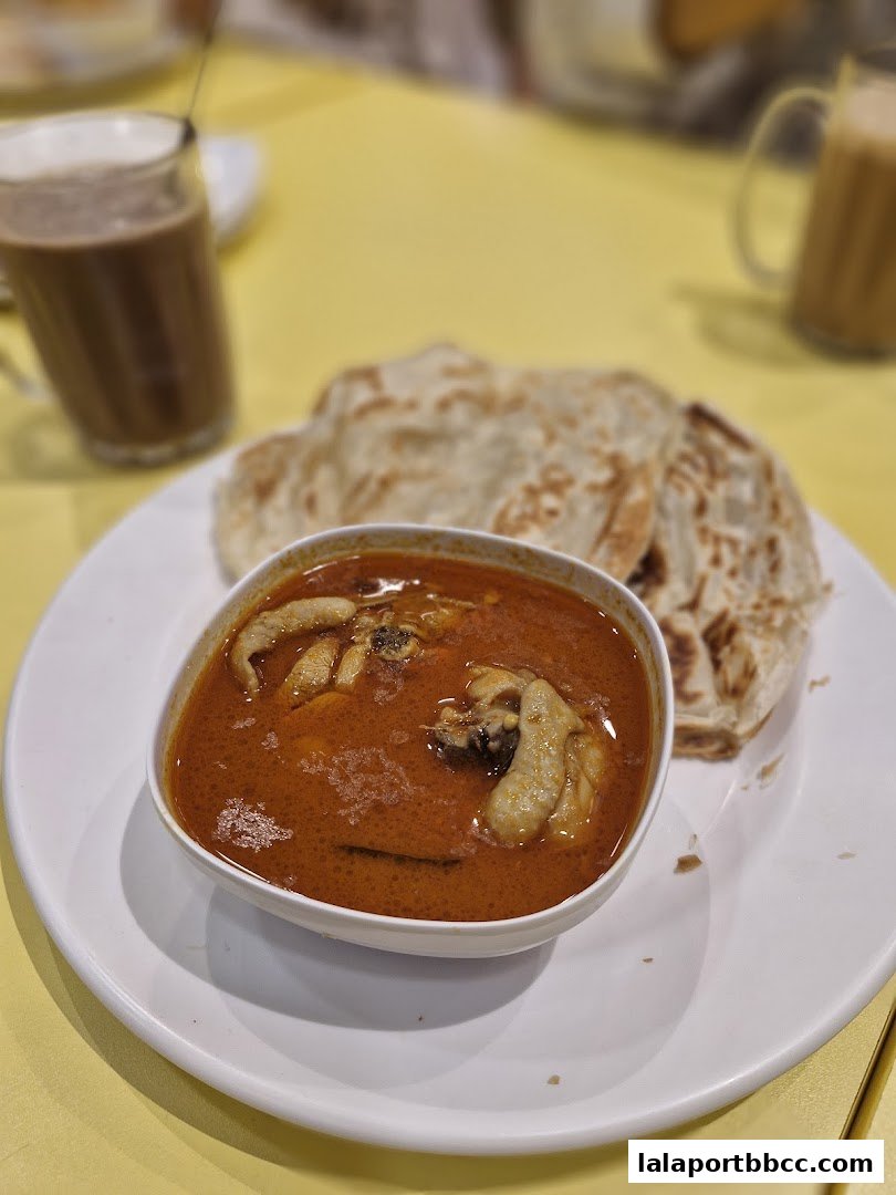A plate of Roti Canai with chicken curry and two glasses of teh tarik.