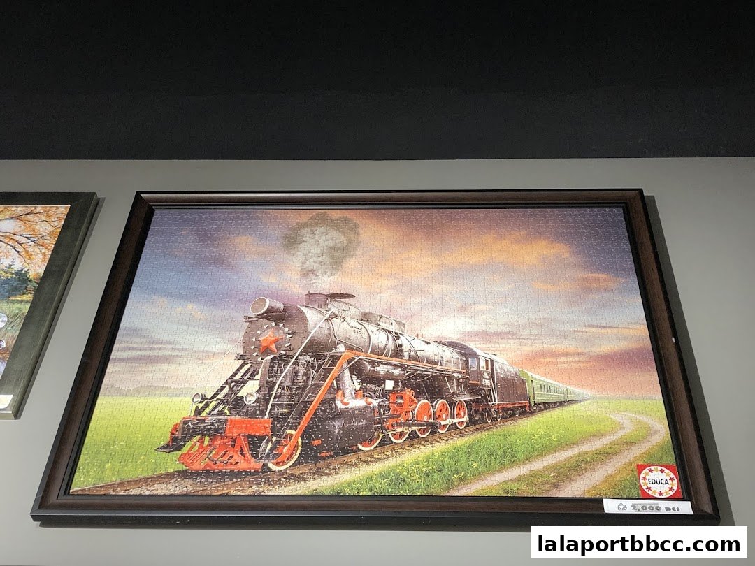 A framed jigsaw puzzle of a steam train on a track at sunset.