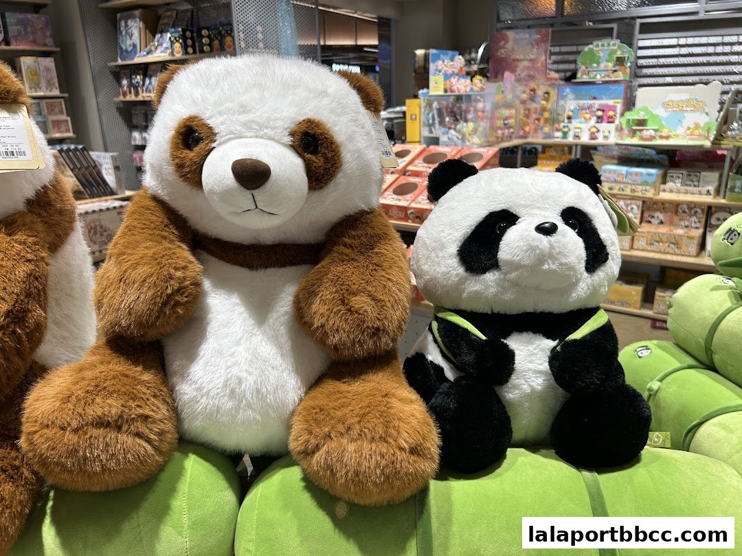 Two adorable panda plush toys are displayed in a store, with shelves of merchandise in the background.