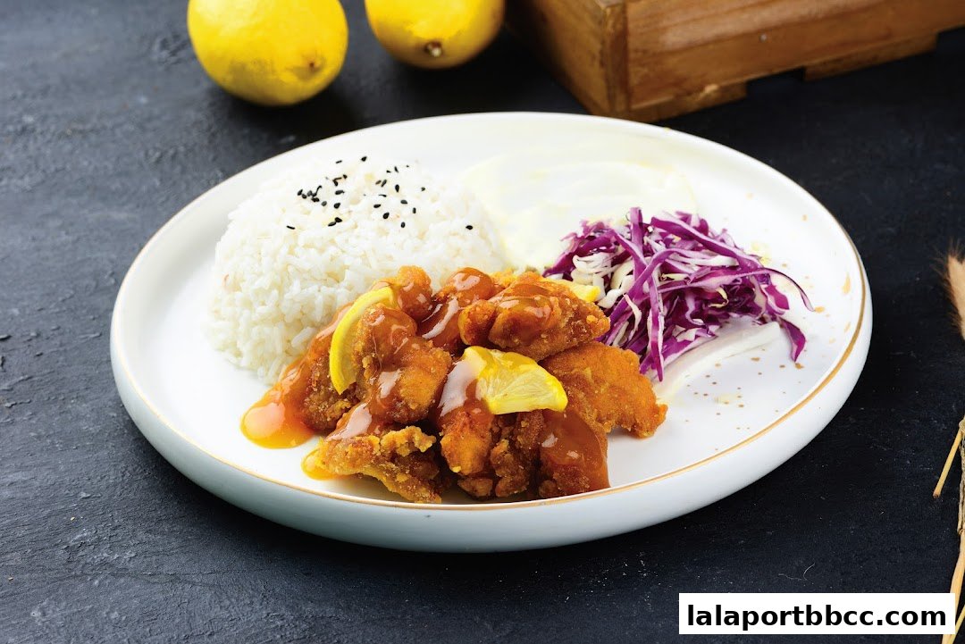 A plate of crispy fried chicken with lemon sauce, rice, and shredded cabbage.