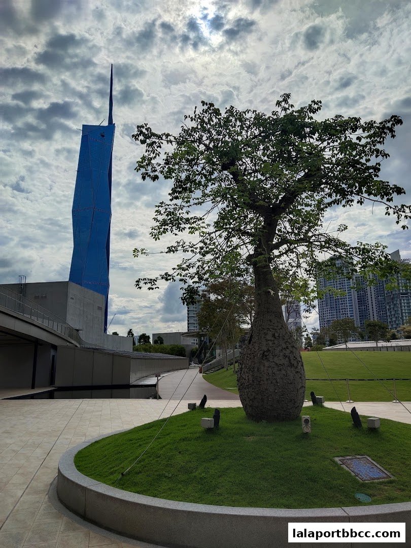 A striking blue tower stands tall against a cloudy sky, with a large tree in the foreground.