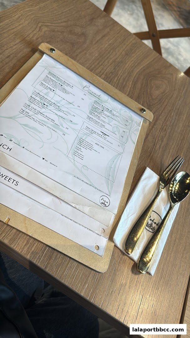 A menu from POKOK LaLaport with brunch and sweets options, alongside cutlery.