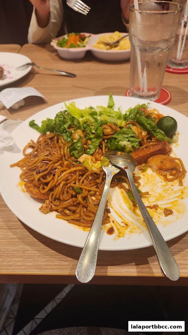 A plate of noodles with salad and cutlery on a wooden table.