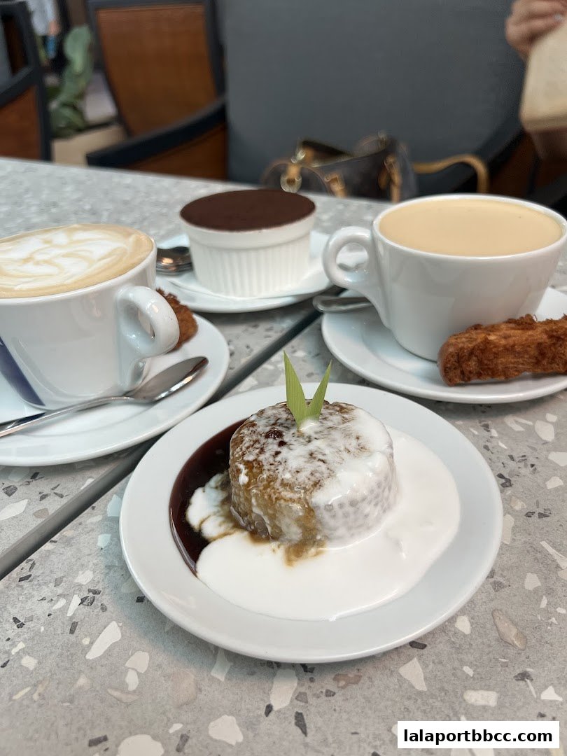 A close-up of three desserts and two coffees on a speckled table.