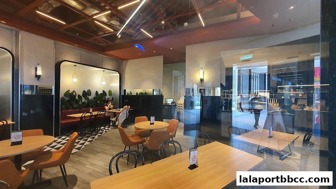Interior view of a modern cafe with orange chairs and wooden tables, featuring a green wall.