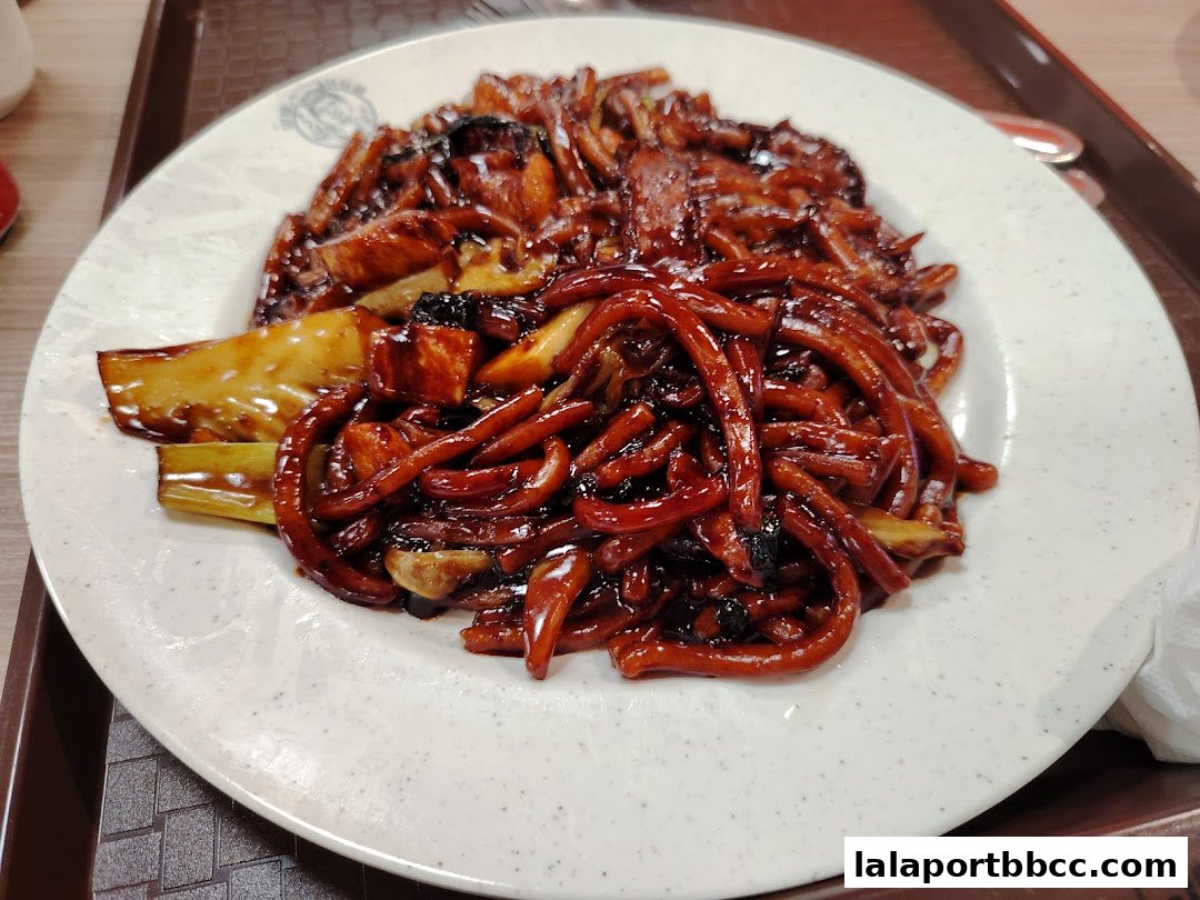 A plate of delicious Hokkien Mee noodles with a rich, dark sauce and visible ingredients.