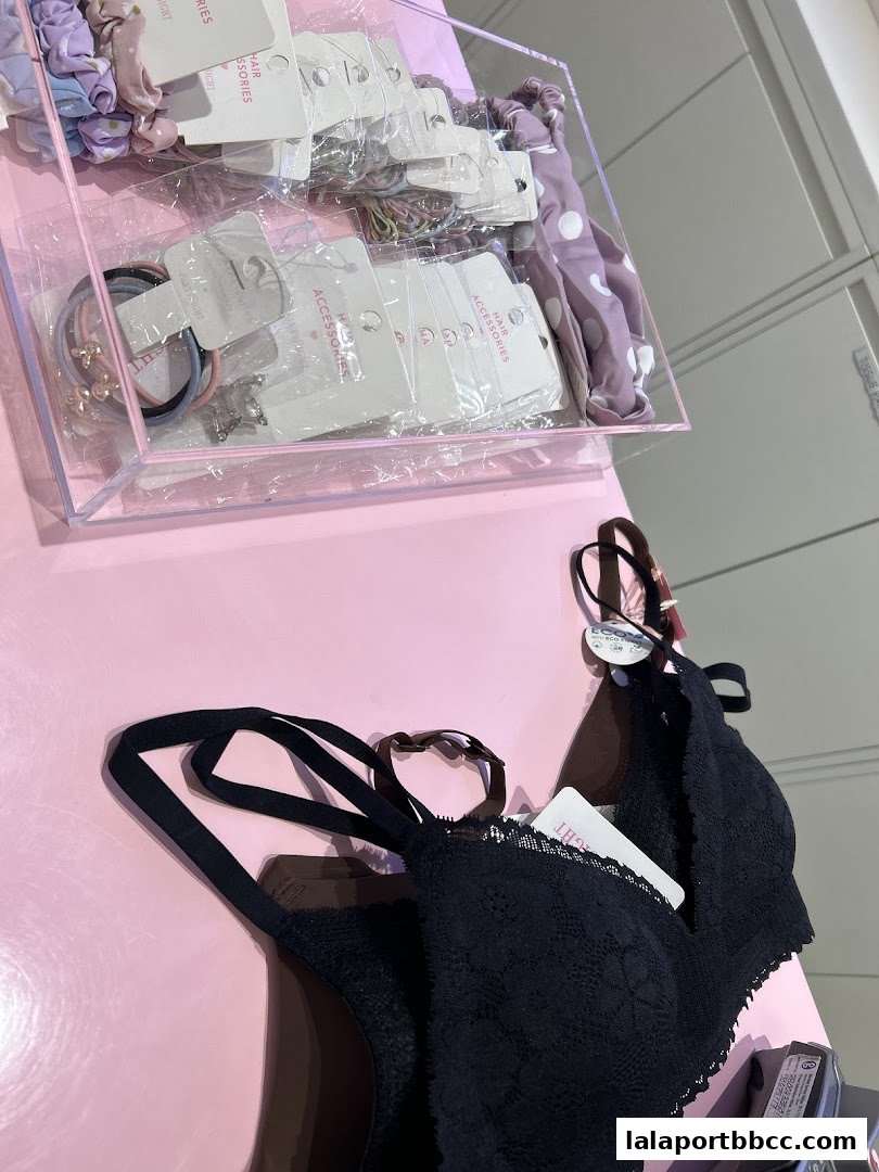 A black lace bra and various hair accessories are displayed on a pink surface.