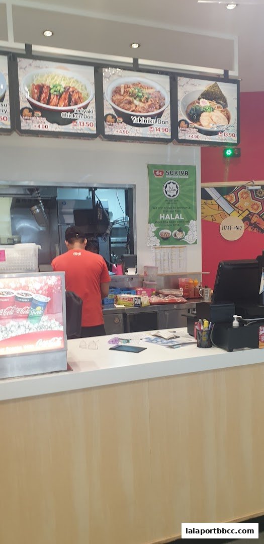 A Sukiya restaurant counter with food displays and a staff member working.