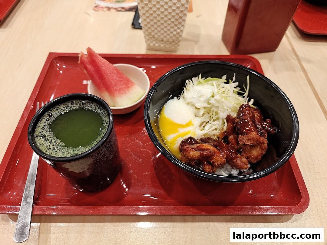A bowl of Japanese rice with chicken, egg, and cabbage, served with a drink and watermelon.