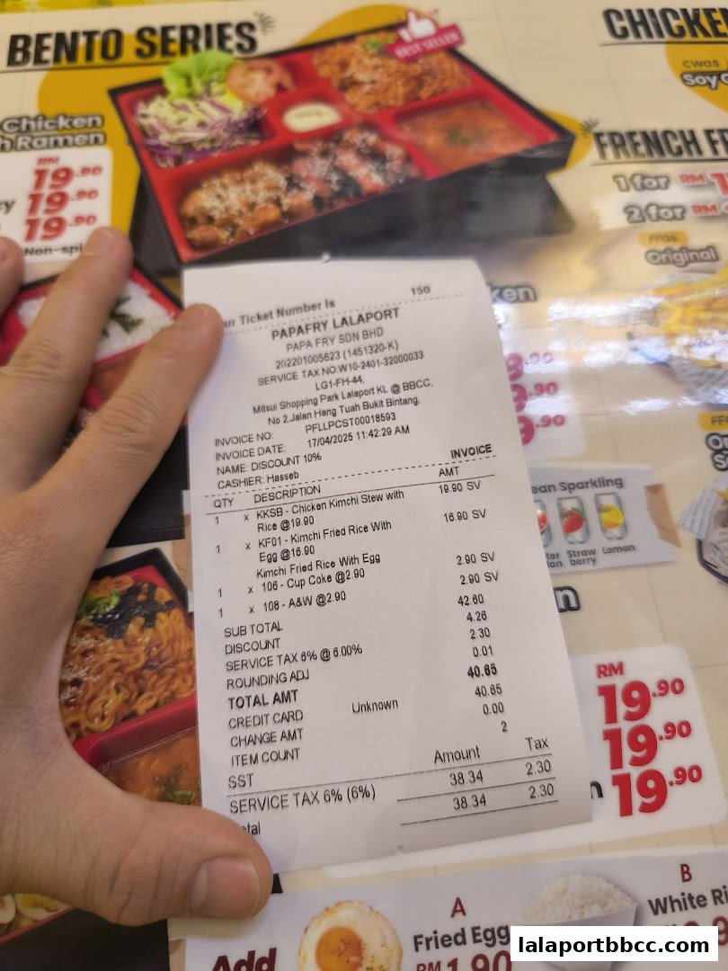 A receipt from PapaFry Lalaport is held over a menu featuring bento boxes and other food items.
