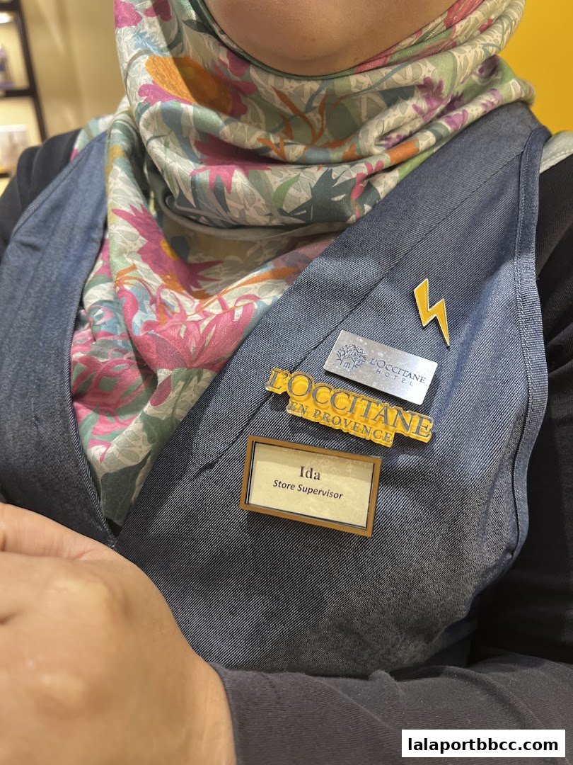 A store supervisor wearing a denim vest and a floral scarf with L'Occitane branding.