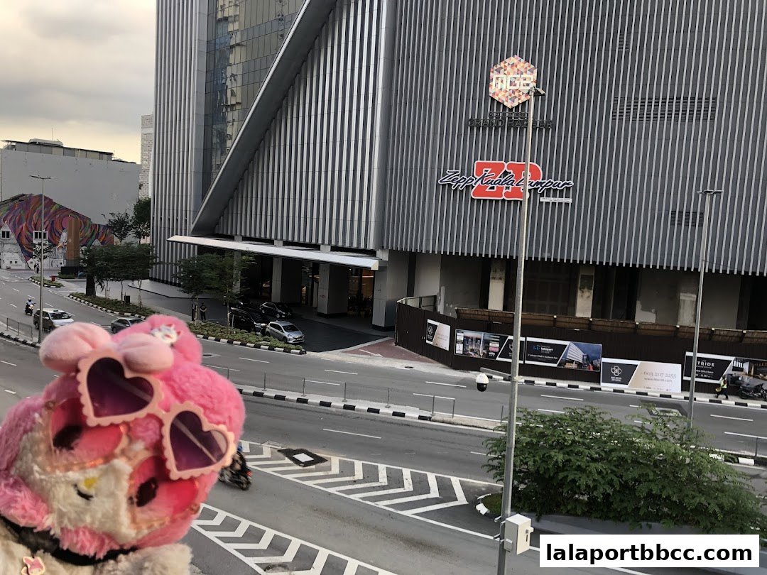 A plush toy with heart-shaped sunglasses in front of the Zepp Kuala Lumpur building.